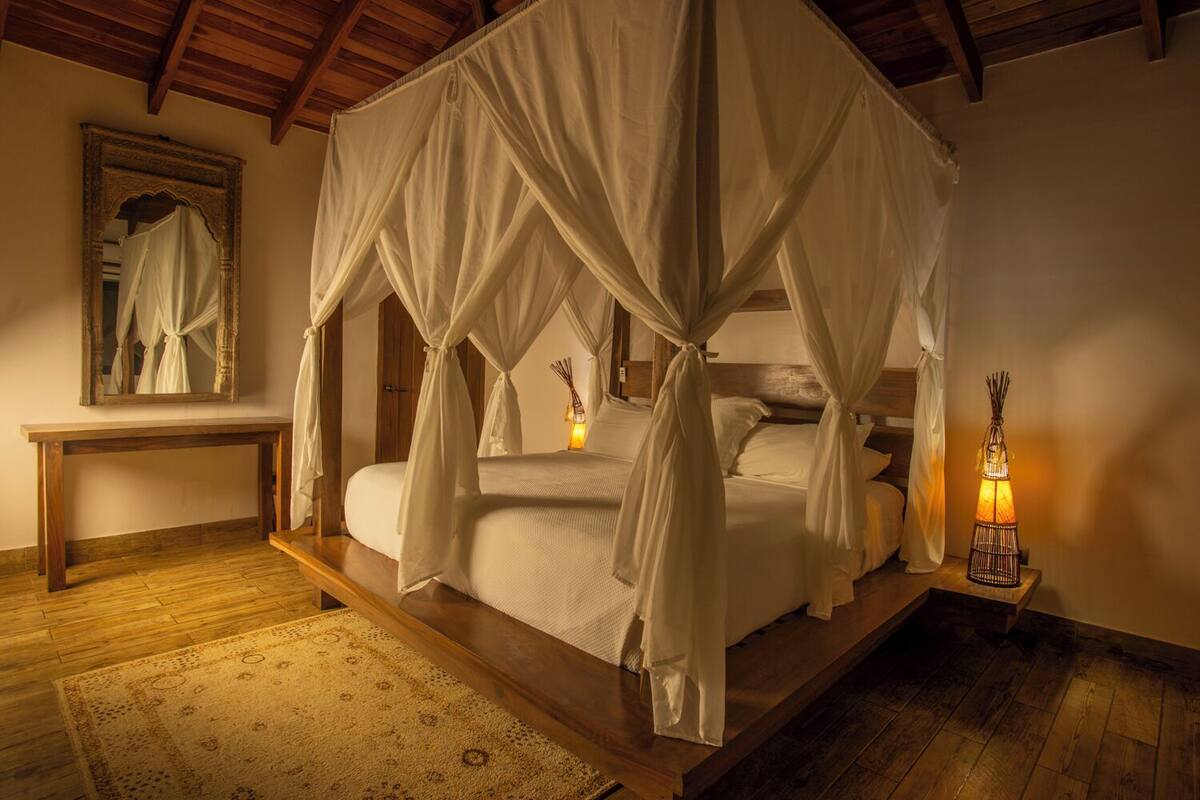 Un lit à baldaquin à quatre poteaux, doté d’une plateforme en bois, d’une table de chevet, d’un miroir et d’une lanterne décorative.