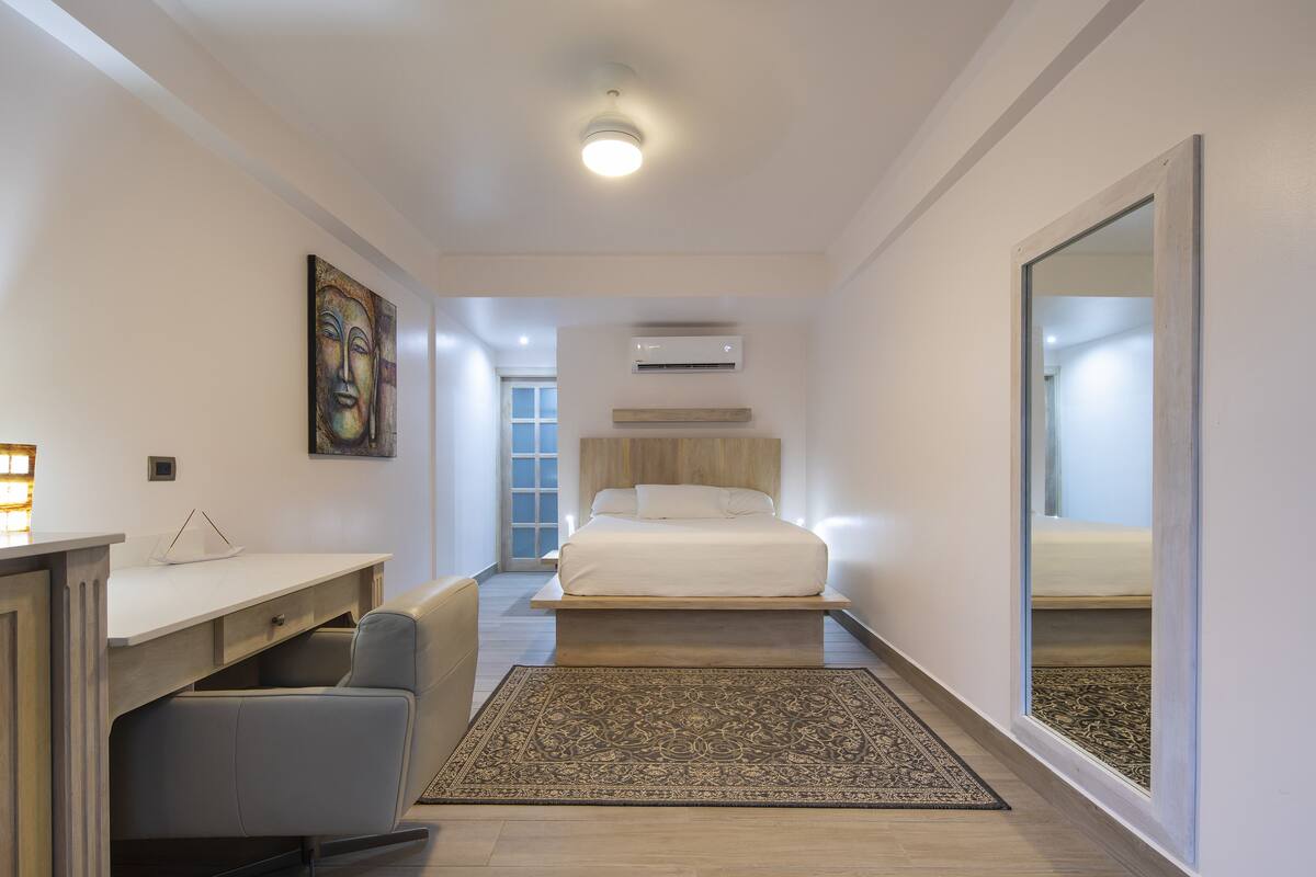 Une chambre d’hôtel moderne équipée d’un lit, d’un bureau et d’une chaise, d’un grand miroir et d’un tapis à motifs.