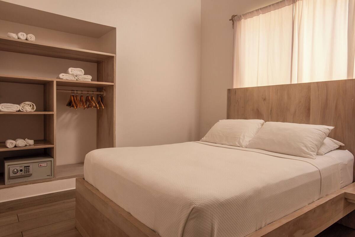 Une chambre à coucher comprenant un lit, une tête de lit en bois, une armoire contenant des serviettes et un panneau de commande.