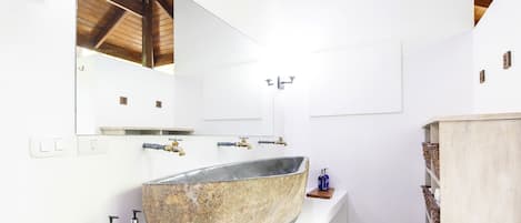 A bathroom with a large stone sink, wooden shelves, and a mirror.