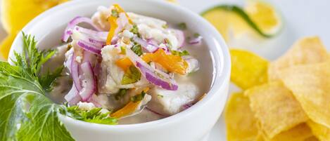 Un plato de ceviche con cebolla roja, cilantro y lima, acompañado de totopos.