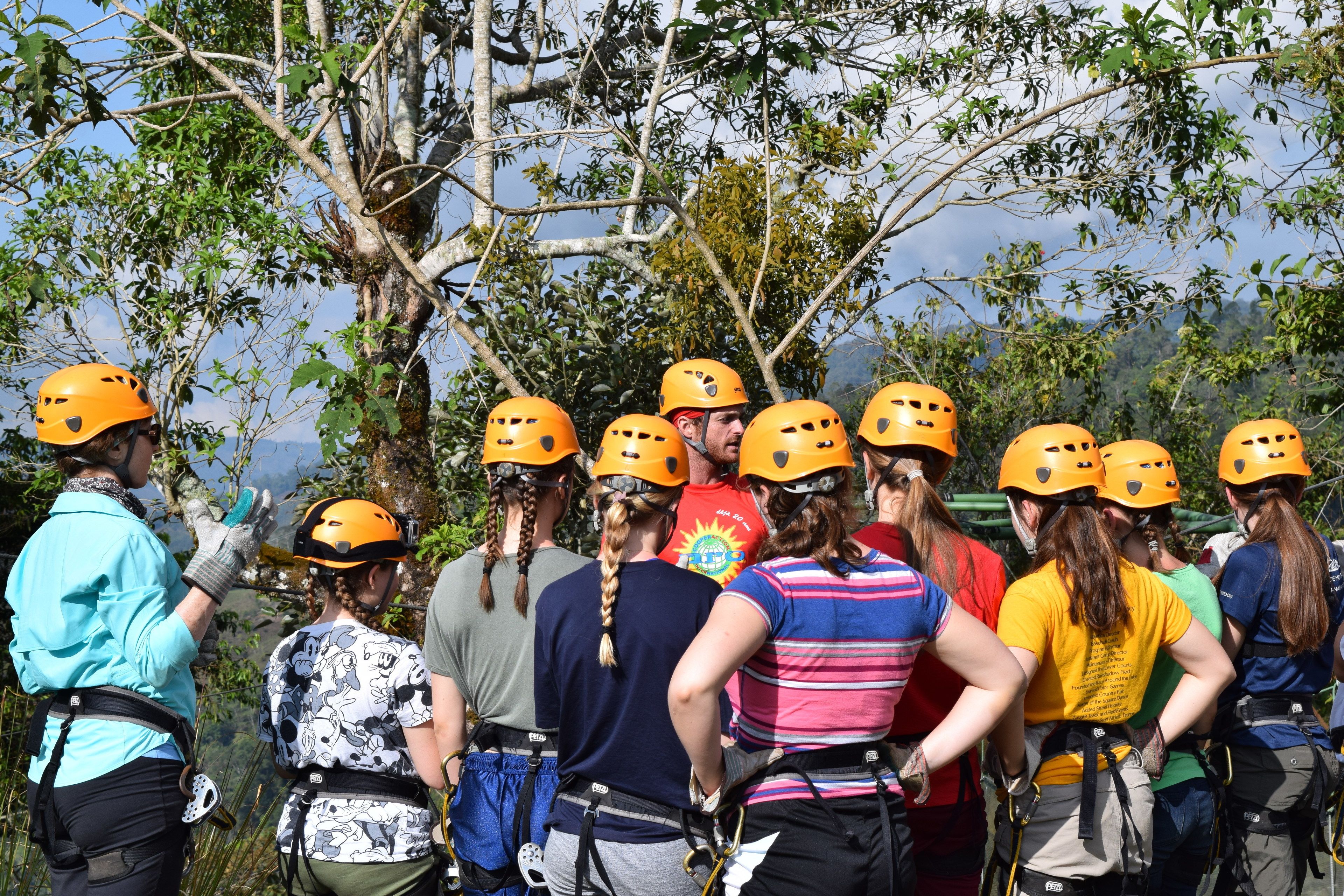 A group of people wearing helmets and harnesses, standing in a line outdoors.