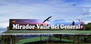A billboard advertising 'Mirador Valle del General' with a scenic view of a valley and a bird in flight. - Mirador Valle del General (Páramo)