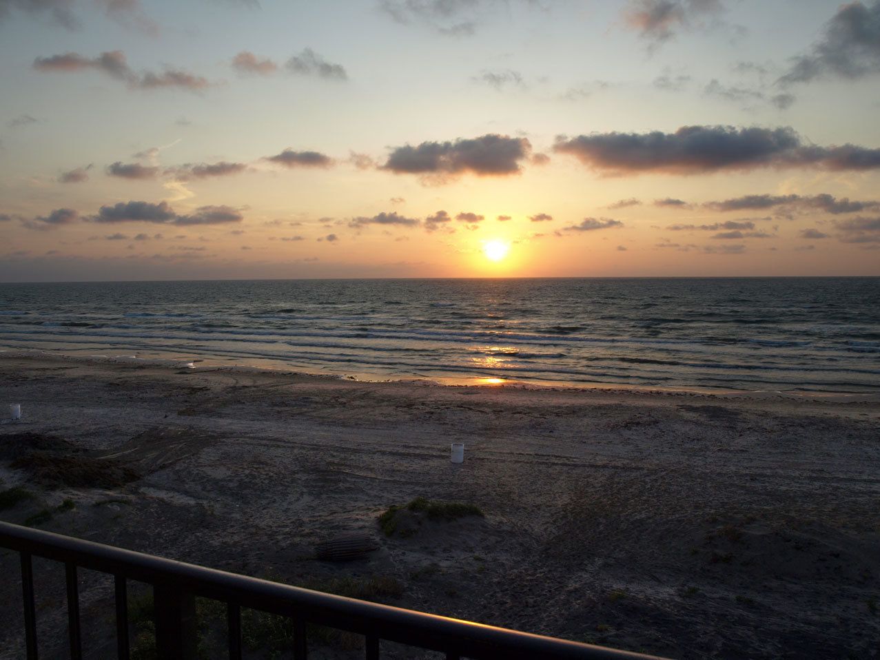A beach at sunset with a railing in the foreground.