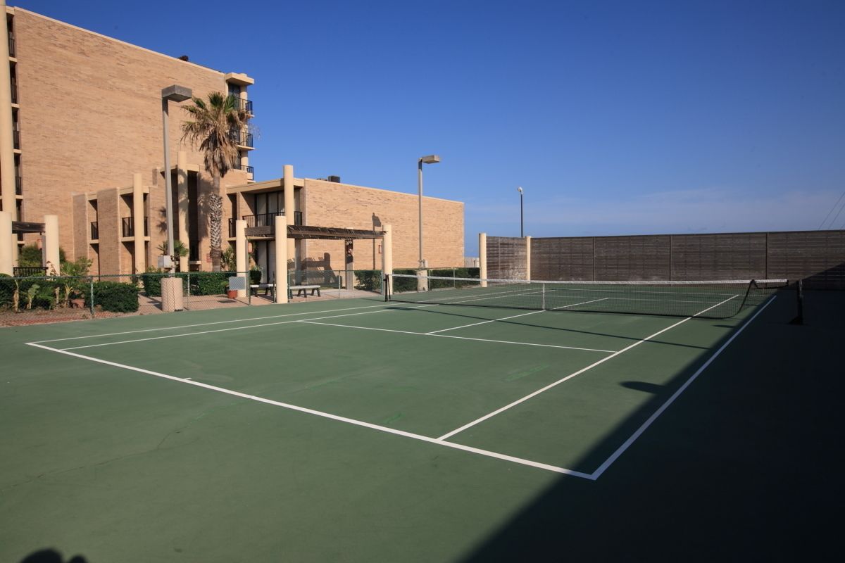 Una cancha de tenis al aire libre junto a un edificio con varios pisos y balcones.