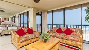A room with a bed, two sofas with red cushions, a wooden coffee table, and a ceiling fan. - Sea Vista by South Padre Condo Rentals (South Padre Island)