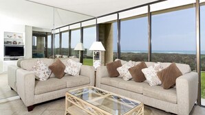 A modern living room with two sofas, a glass coffee table, and large windows offering a view of the ocean. - Sea Vista by South Padre Condo Rentals (South Padre Island)