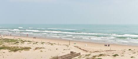 A sandy beach with a wooden boardwalk leading to the water, and a few people walking along the shore.