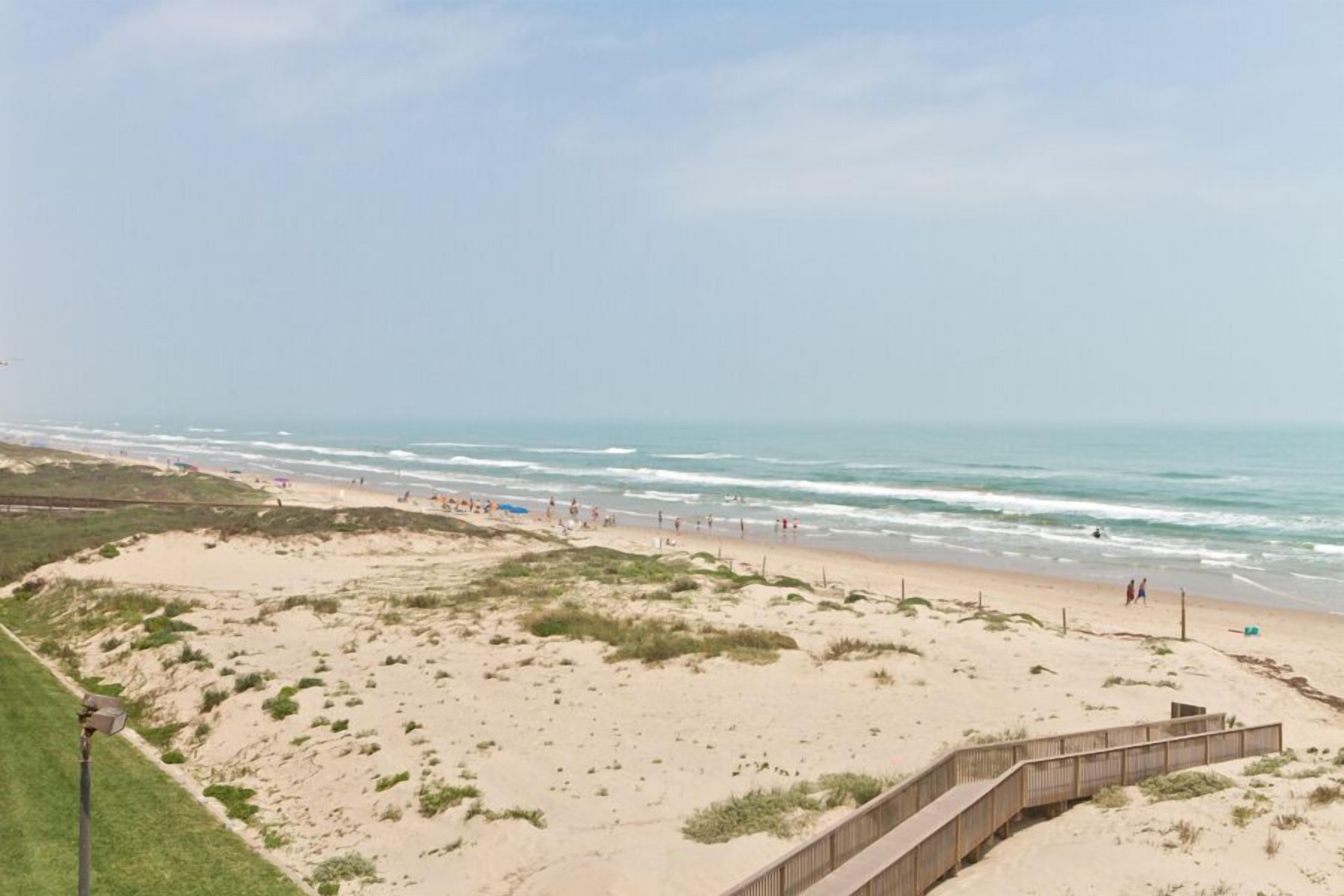 Una playa con un paseo marítimo de madera que conduce a la orilla, dunas de arena y el océano.