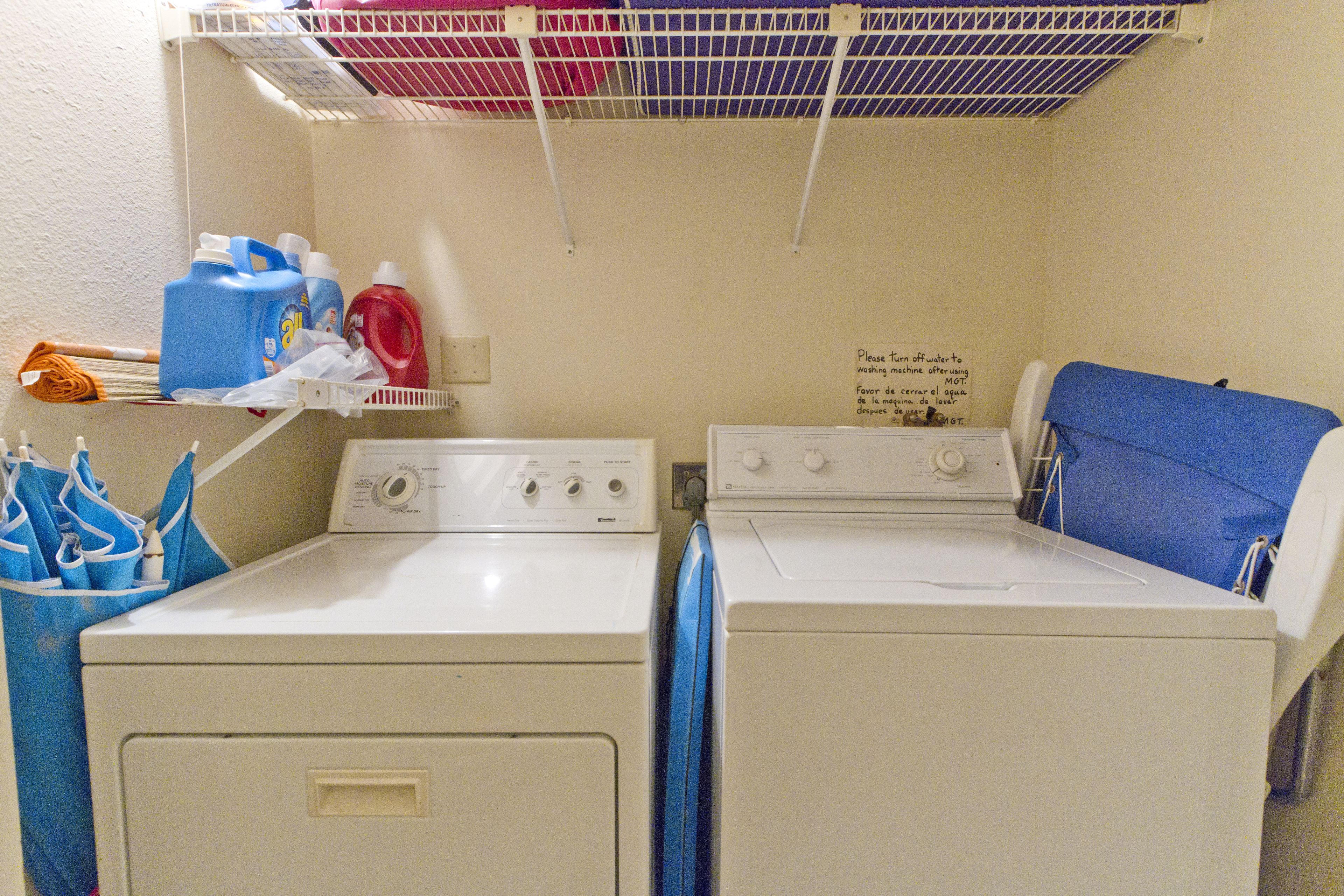 A laundry area with two washing machines, a shelf with detergent bottles, and a sign indicating the use of a washing machine.