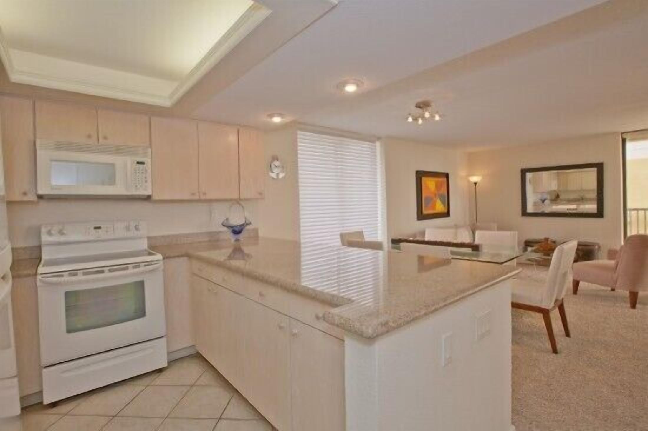 A modern kitchen with white cabinets, a built-in microwave, and an oven. There is a dining area with a glass table and chairs.