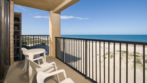 A balcony with a view of the beach, a table, and two chairs. - Sea Vista by South Padre Condo Rentals (South Padre Island)