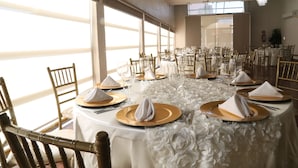 Un salón de banquetes con mesas redondas dispuestas para un evento formal, con manteles blancos y detalles dorados.