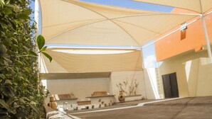 Un área de patio al aire libre con un amplio toldo, una pared de piedra y un edificio con una puerta al fondo.