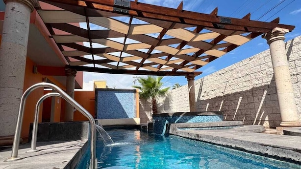 Una piscina con una estructura de pérgola, paredes de piedra y una palmera.