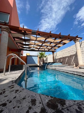 A swimming pool with a pergola structure, stone walls, and a palm tree. - Copper Canyon Boutique Hotel (Chihuahua)