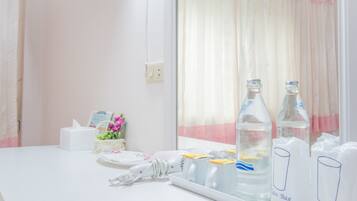 A hotel room with a white counter, a hairdryer, a basket with flowers, and two bottles labeled "Glass Bag".