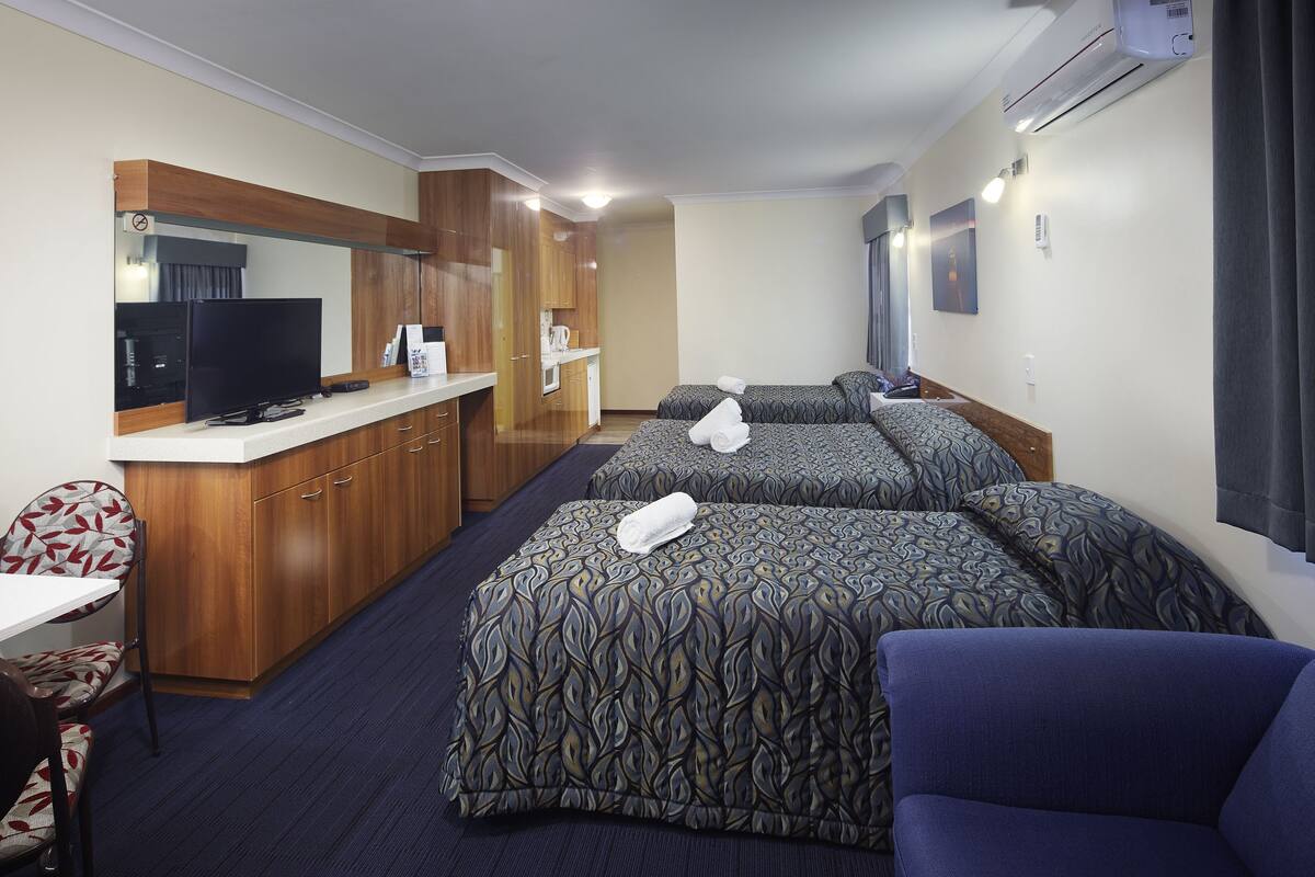 Ein Hotelzimmer mit Küchenzeile, einem Fernseher, zwei Betten mit gemusterten Bettbezügen, einem blauen Sofa und einem Spiegel.