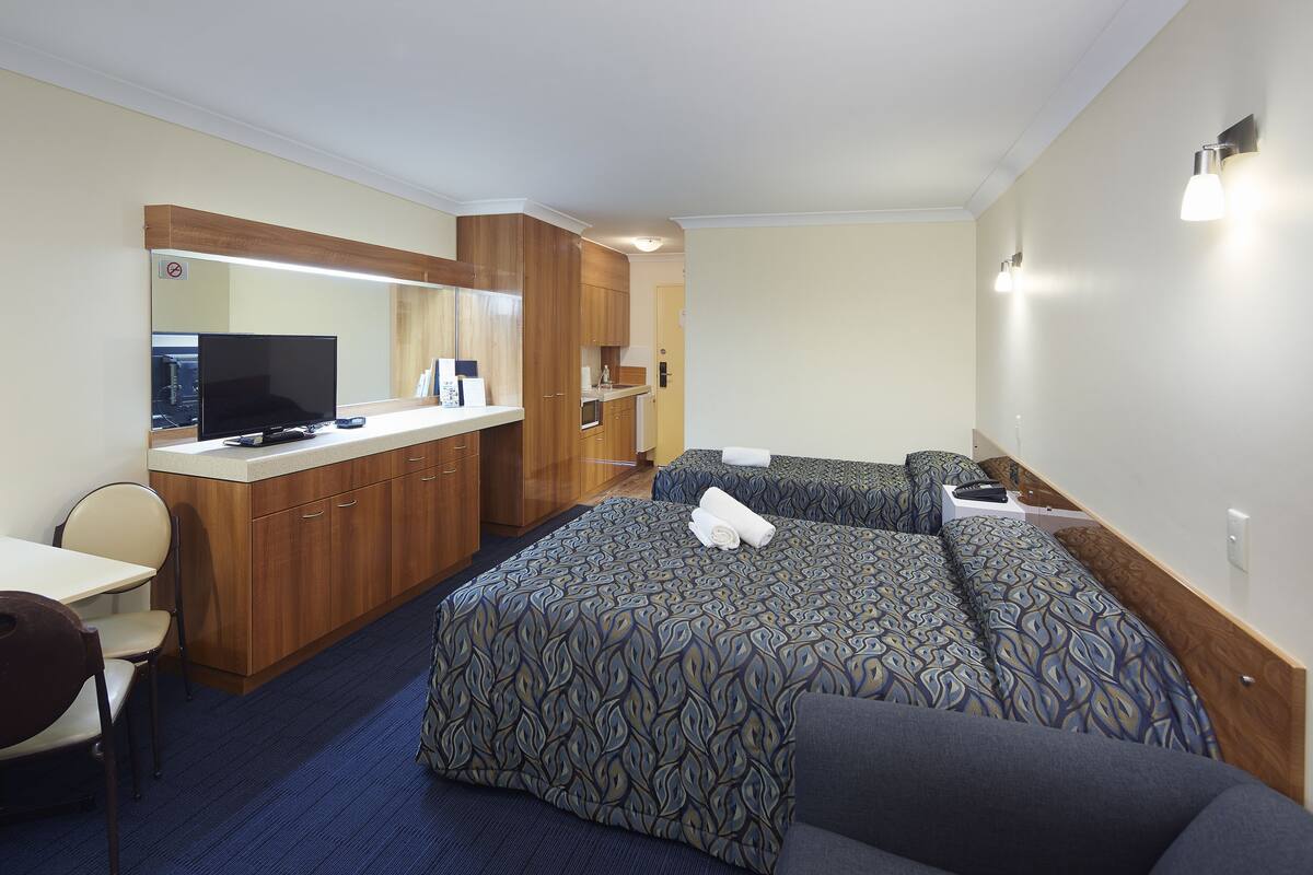 Ein Hotelzimmer mit Bett, Schreibtisch, Stuhl, Fernseher und einer Küchenzeile.