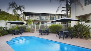 A swimming pool with a tiled deck, surrounded by outdoor furniture and umbrellas.