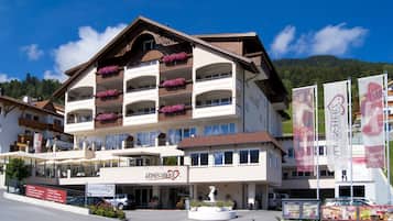 Ein mehrstöckiges Hotel mit Balkonen, die mit Blumen geschmückt sind, einem zentralen Eingang und einer Fontäne.