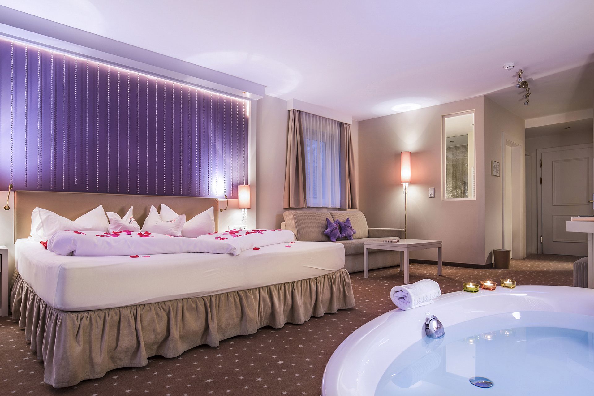 Une chambre d’hôtel avec un lit, un canapé, une petite table, une baignoire et un miroir.