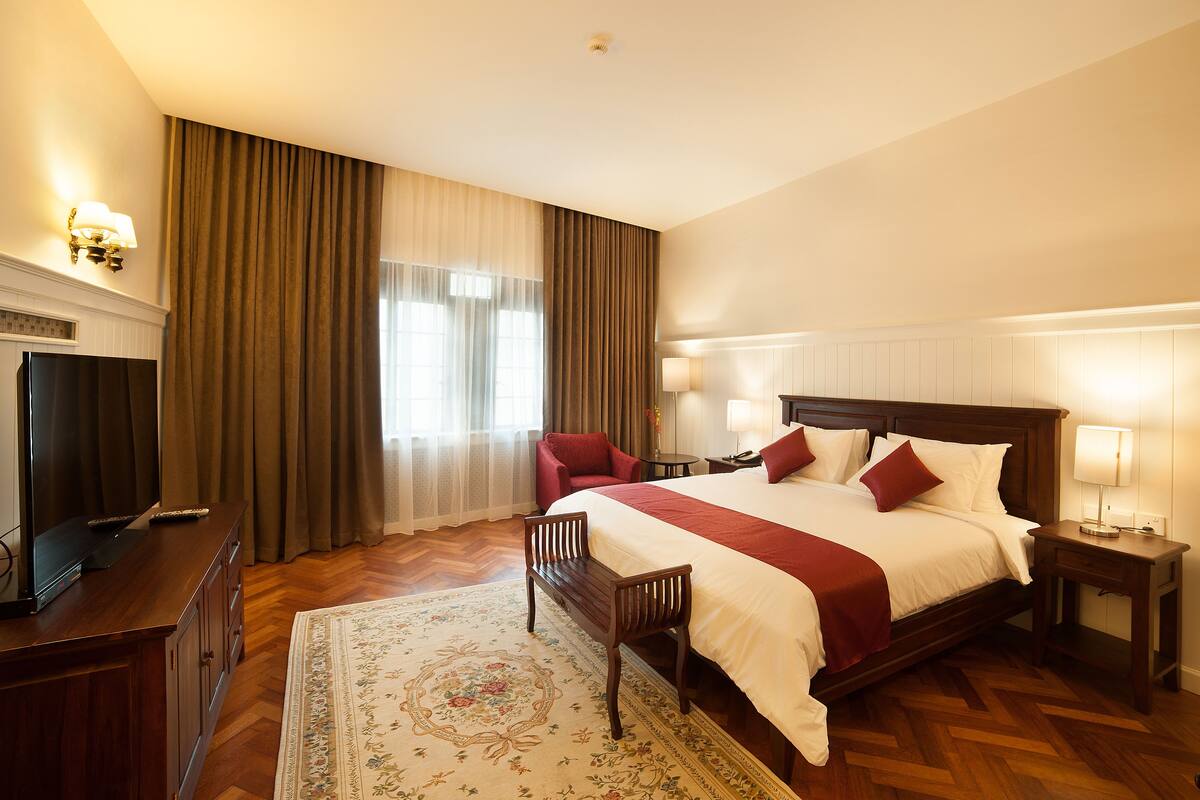 A hotel room with a large bed, a TV, a bench, and a desk.