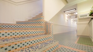 A staircase with a patterned tile design, leading to a landing with a light fixture and a wall-mounted TV. - The Chambers (George Town)