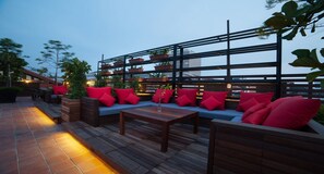 An outdoor seating area with wooden furniture, red cushions, and planters on a wooden deck. - The Chambers (George Town)