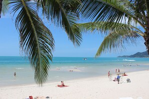 A beach with palm trees, clear blue water, and boats. - Banana Fan Sea Resort (Koh Samui)