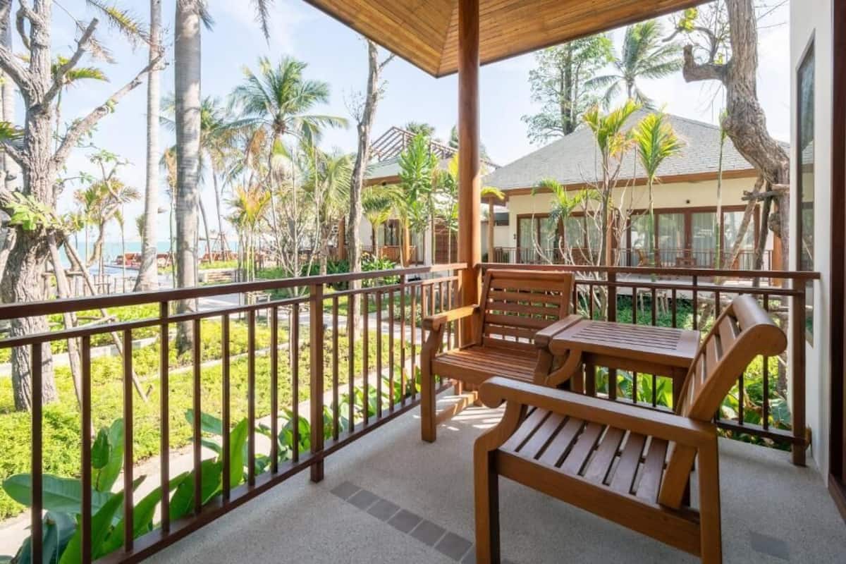 A wooden bench and table on a balcony with a view of palm trees and a building in the background.