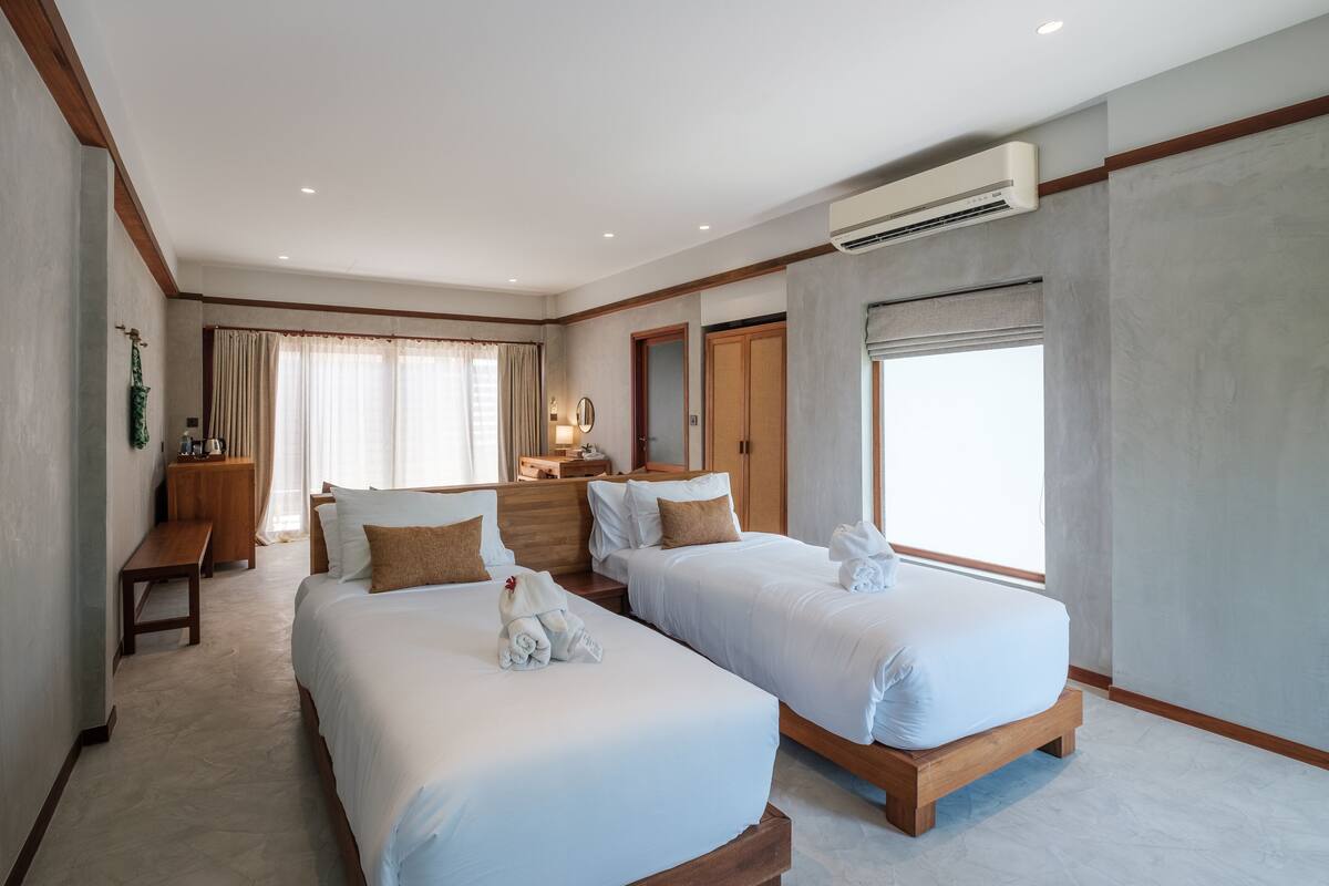 A hotel room with two beds, a desk, a chair, and a window with curtains.