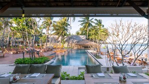 Ein Essbereich am Pool mit Tischen für zwei Personen, mit Blick auf einen Pool und einen Strand.