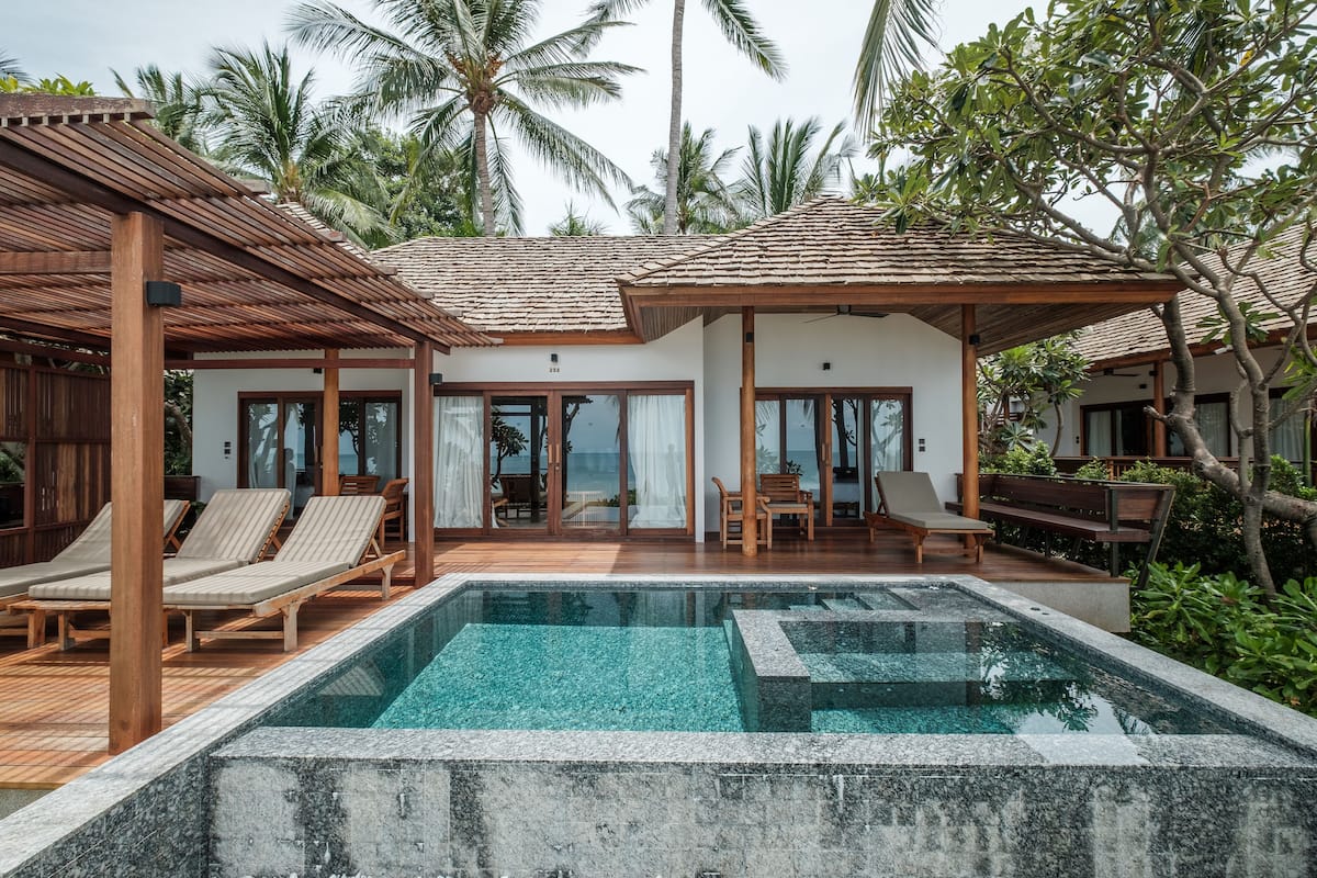 A poolside area with lounge chairs, a wooden deck, and a view of the ocean.