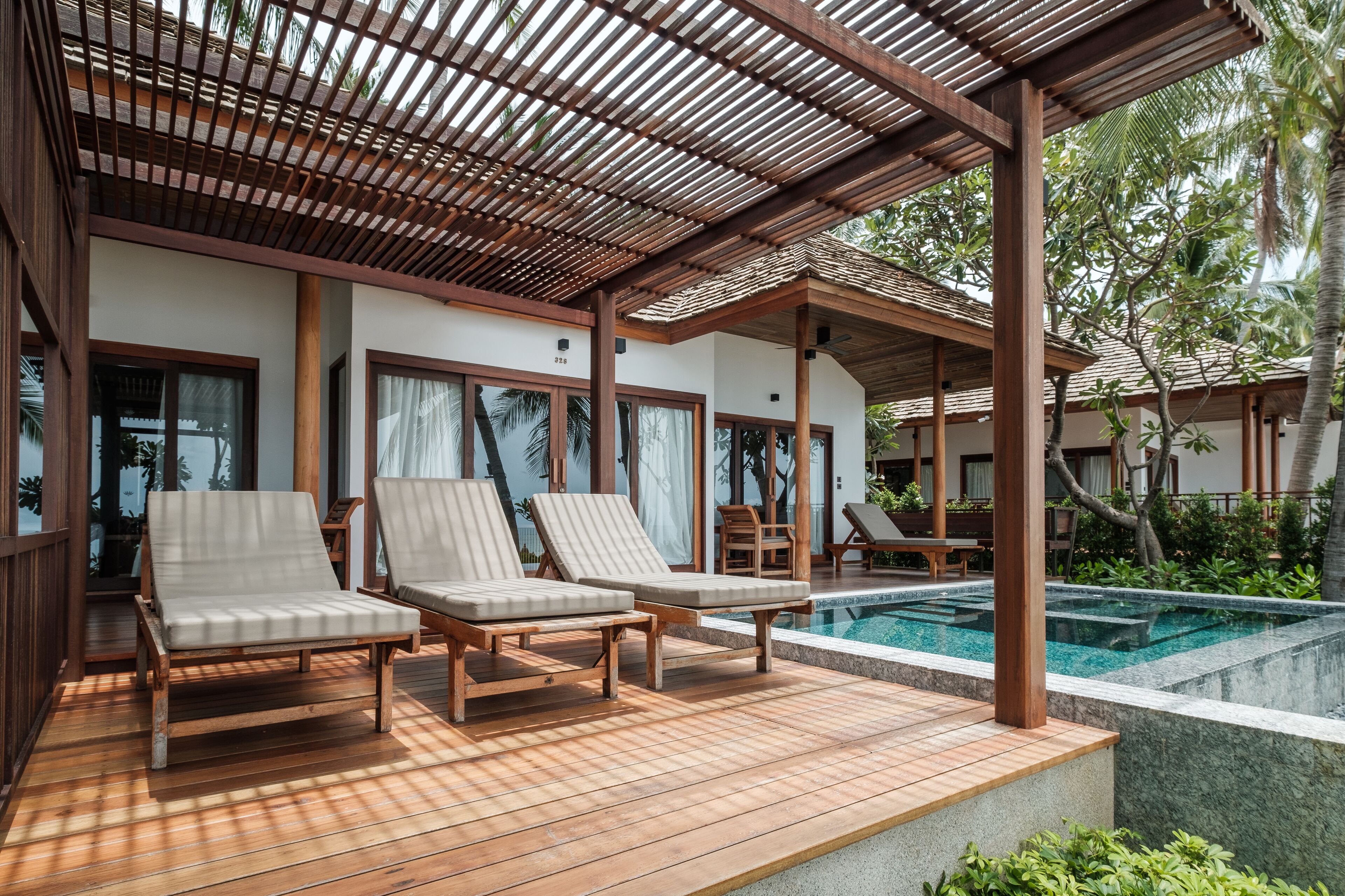Zona de piscina con terraza de madera, sillas de descanso y un área de estar cubierta.