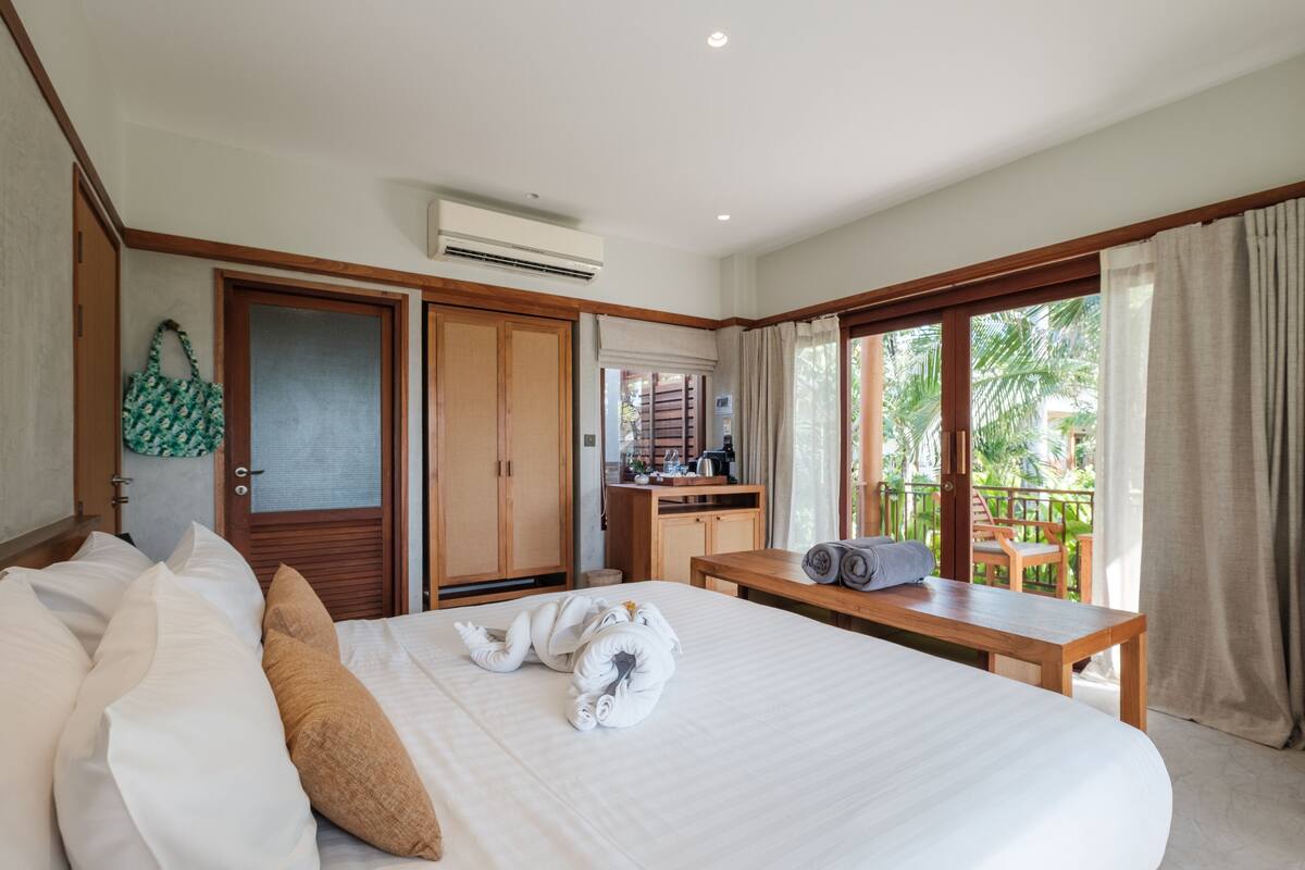 A hotel room with a large bed, a wooden desk, and a balcony with a view of palm trees.