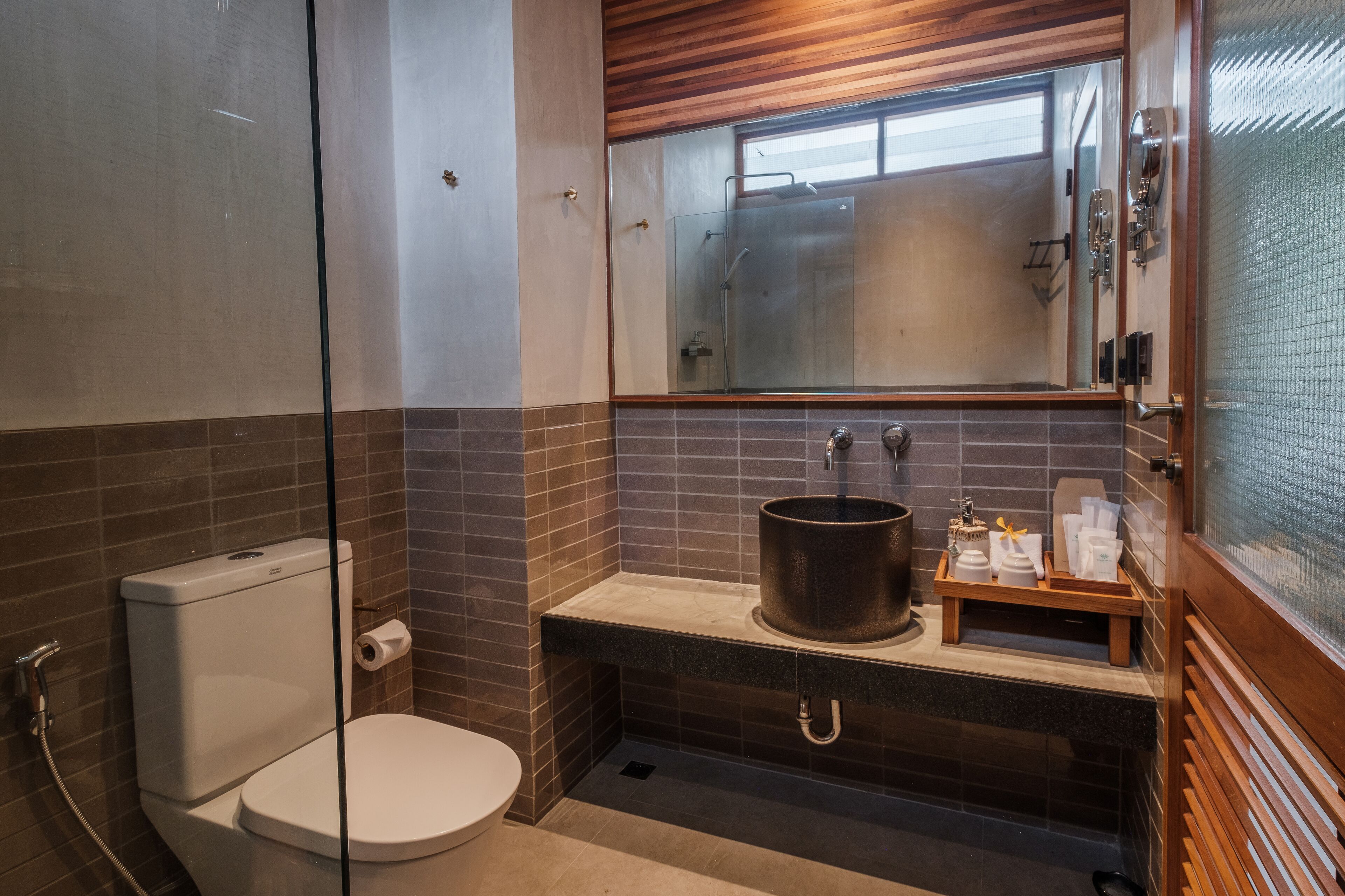 A modern bathroom with a glass-enclosed shower, a toilet, and a sink with a large pot.