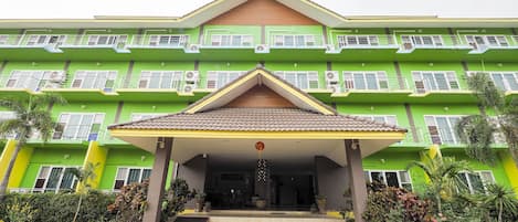A multi-story building with a green facade, a central entrance with a ramp, and a tiled roof.