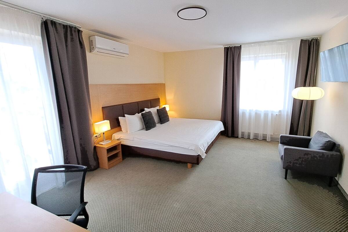 Quarto de hotel com cama, escrivaninha, cadeira, televisão e ar condicionado.