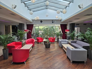 A spacious lobby with modern furniture, a glass ceiling, and potted plants. - POLECZKI RESIDENCE APARTMENTS  (Warsaw)