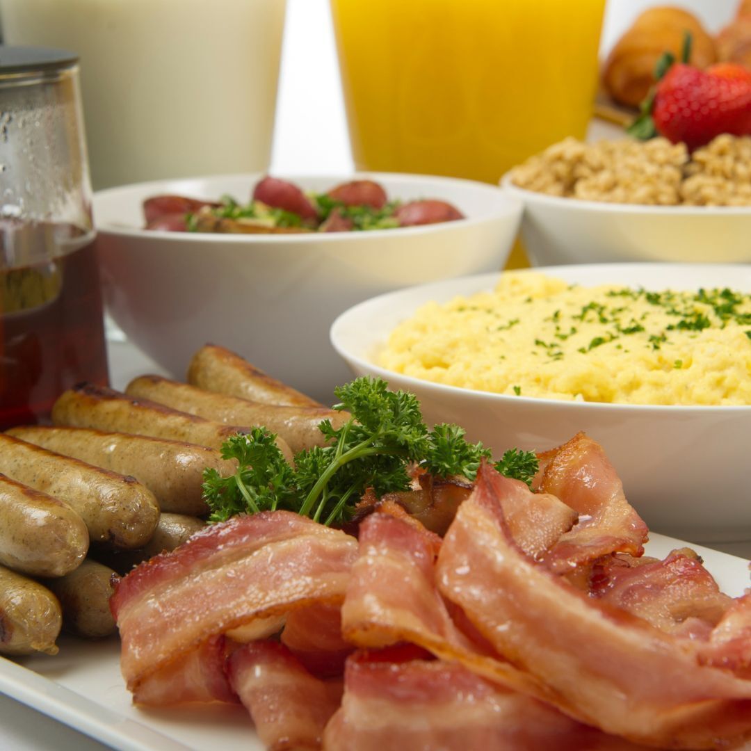 Un plato de desayuno con salchichas, tocino y huevos revueltos.