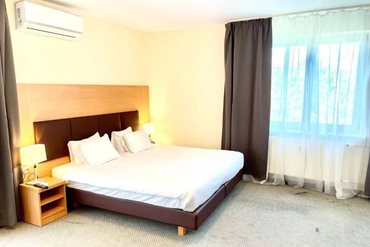 Quarto de hotel com uma cama grande, mesas de cabeceira, ar condicionado e uma janela com cortinas.