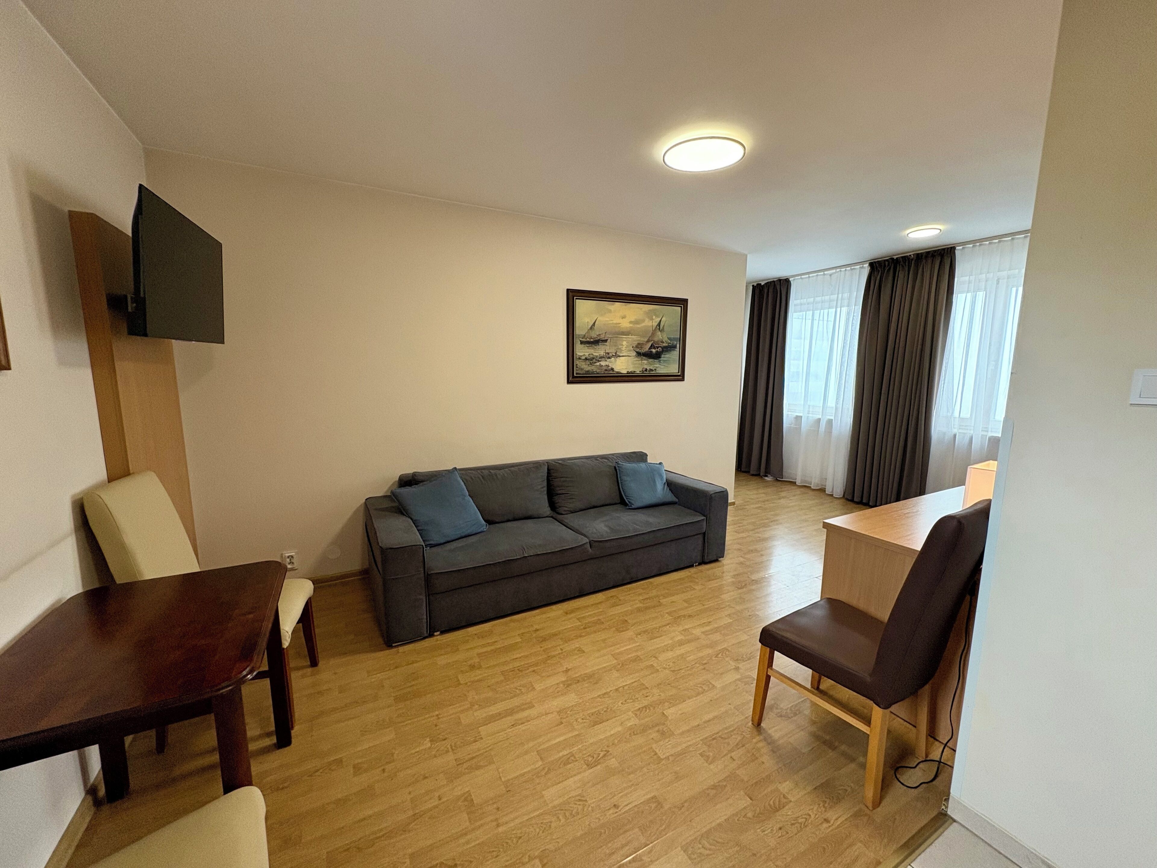A living room with a sofa, a dining table, and a TV mounted on the wall.