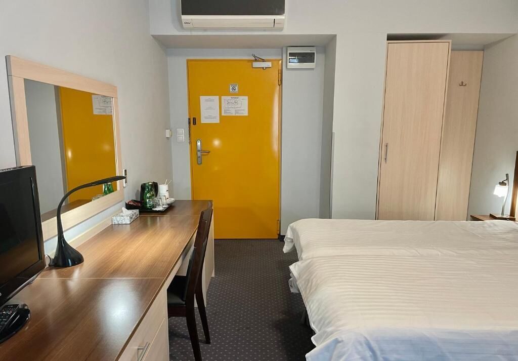 Habitación de hotel con un escritorio de madera, una cama, una puerta amarilla y un armario.