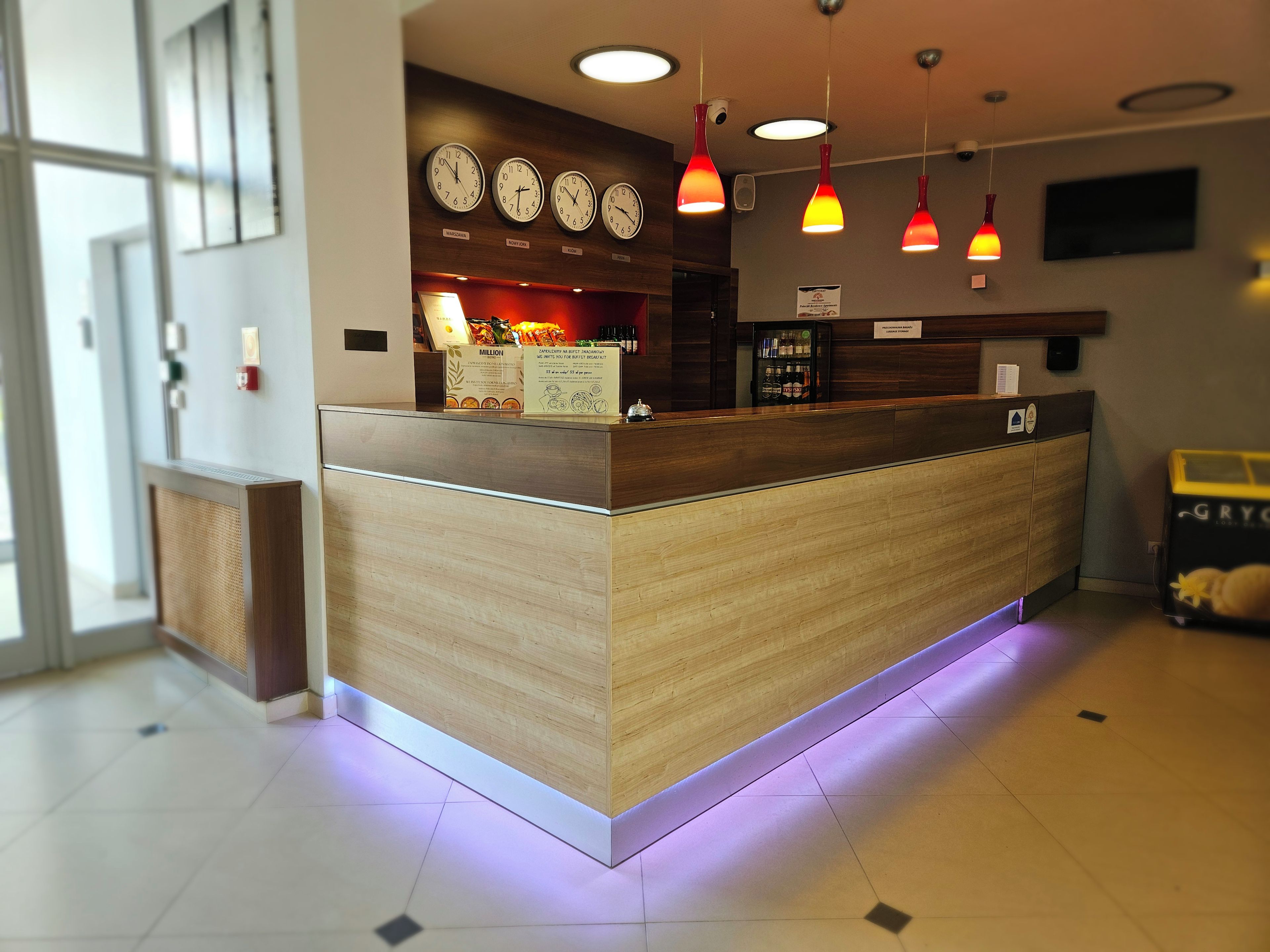 A reception desk with a wooden finish, multiple clocks on the wall, and pendant lighting.