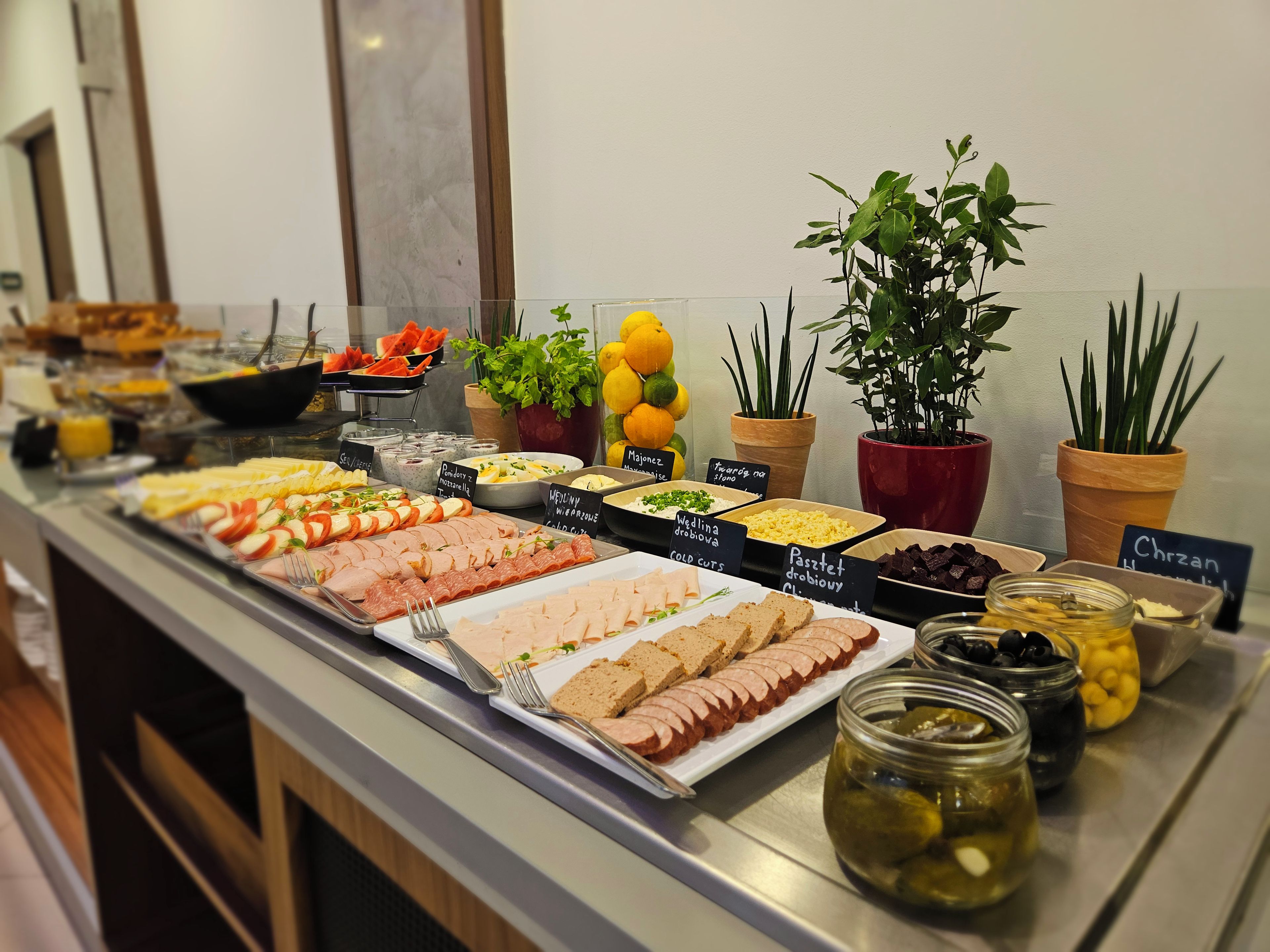 A buffet with various food options and labels, including meats, cheeses, and fruits.