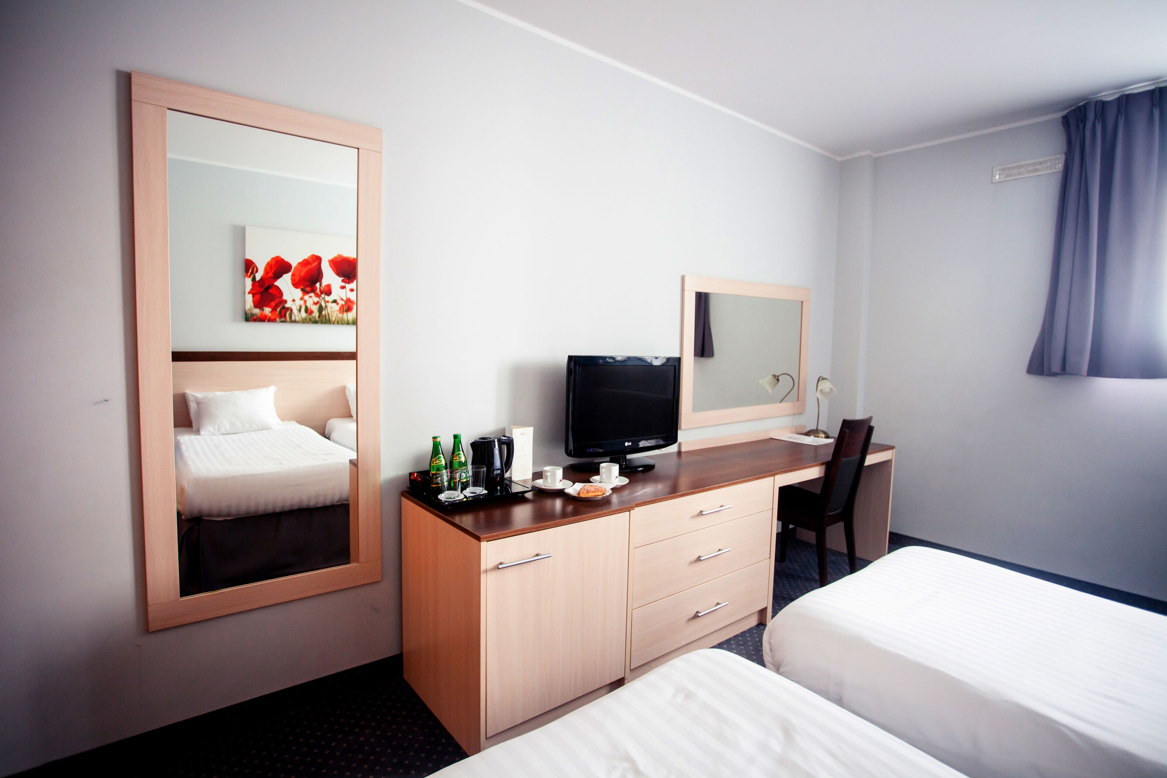 Een hotelkamer met een bed, een bureau met een computer, een televisie en een spiegel.