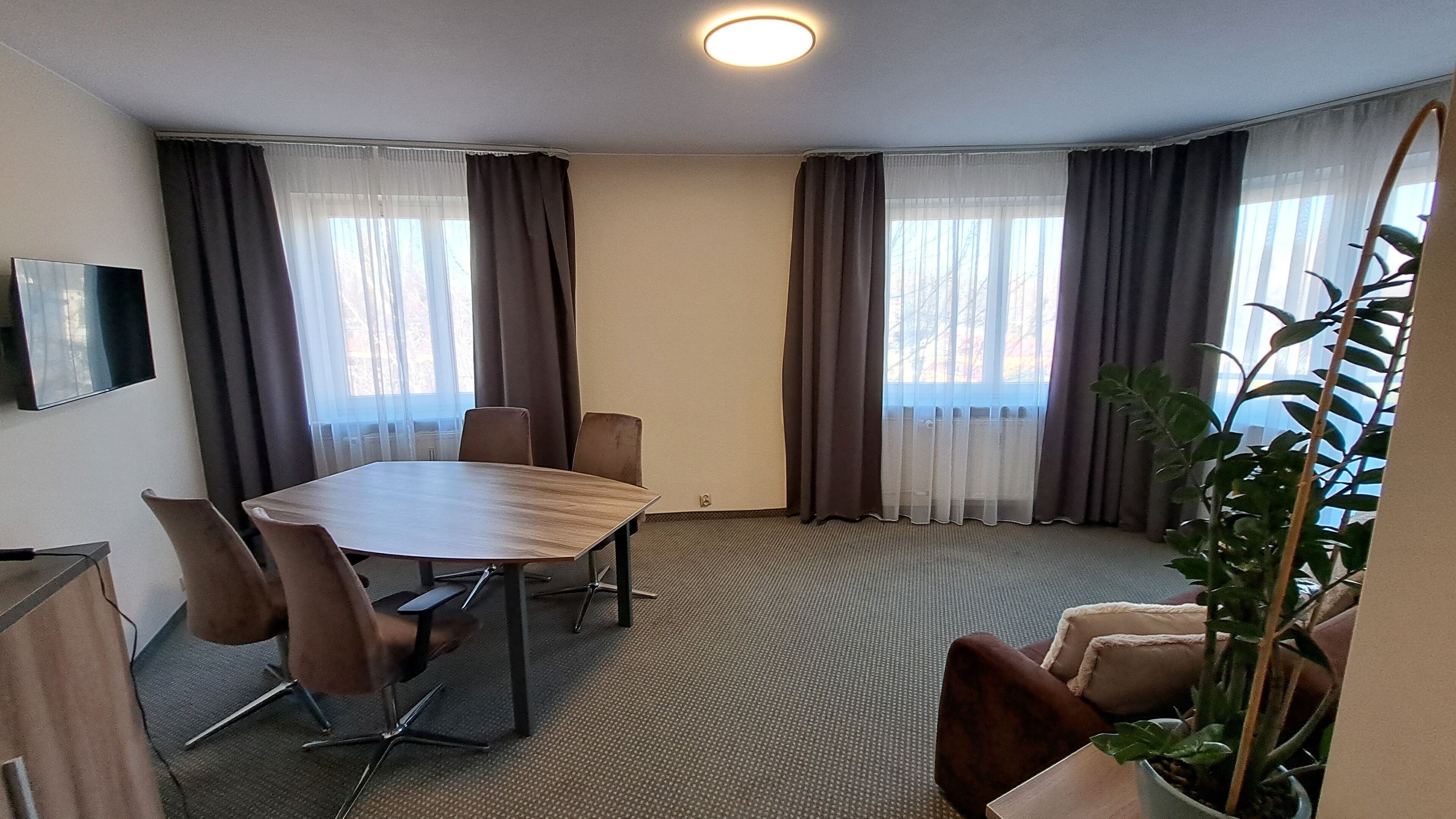 Ein Konferenzraum mit Holztisch, vier Stühlen, einem Flachbildfernseher und großen Fenstern mit Vorhängen.