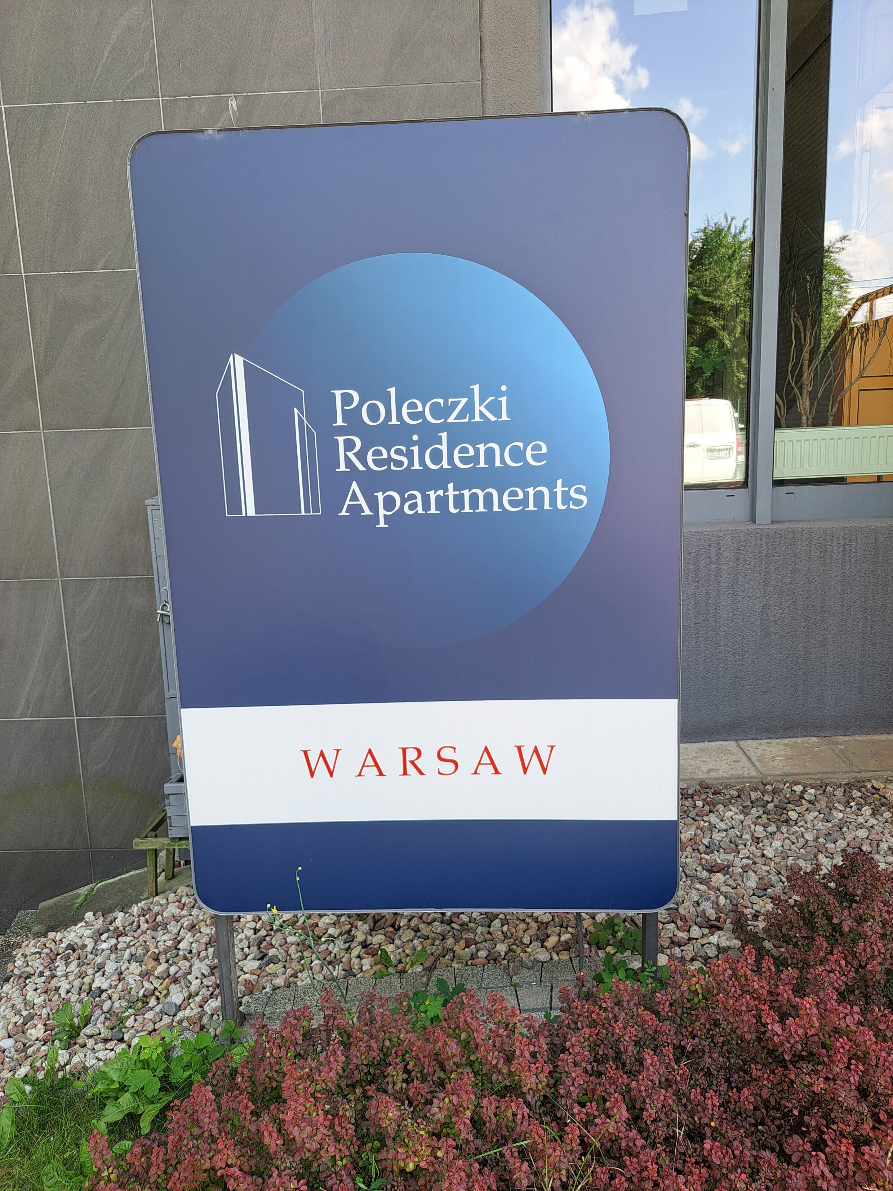 A sign for Poleczi Residence Apartments in Warsaw, featuring a building icon and the location name.