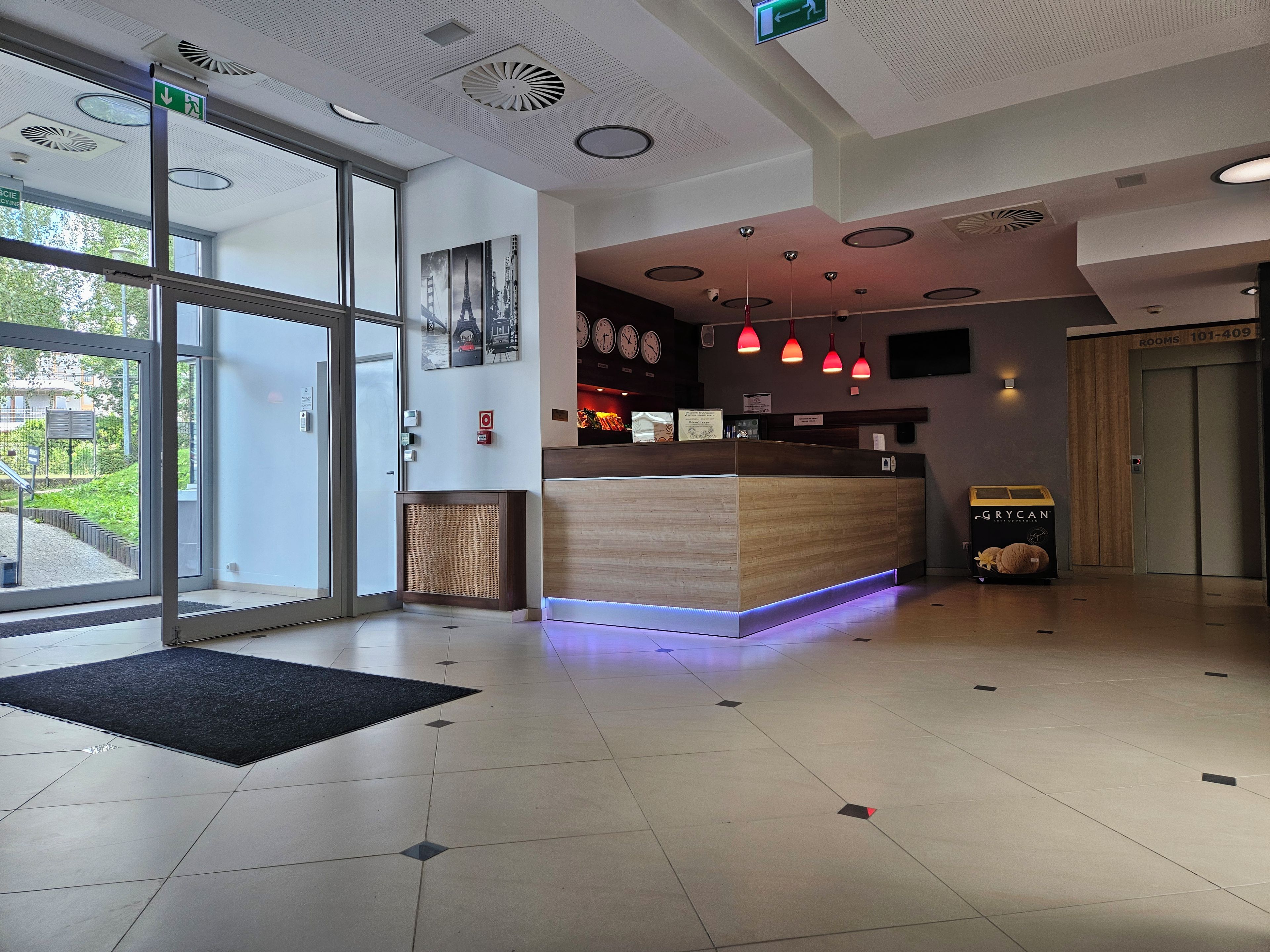 Zona de recepción de hotel con un mostrador, un reloj digital y un detector de incendios.